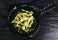 Heap of unpeeled green beans in frying pan on black wooden tabletop — Stock Photo