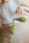 Mani femminili versando frullato verde sano dalla tazza del frullatore in vetro — Foto stock