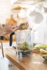 Weibliche Hände legen Kiwi-Früchte in Mixer-Schüssel für grünen Smoothie — Stockfoto