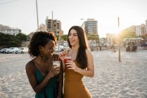 Giovani donne che chiacchierano e ridono con bevande sulla spiaggia sabbiosa della città — Foto stock