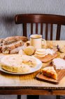 Pastel fresco cortado en plato sobre mesa de madera con tablas de cortar, pan y verduras en rodajas - foto de stock