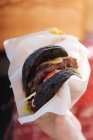 Close-up of black bread bun in hamburger with juice meat patty and pickles — Stock Photo