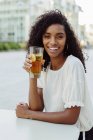 Charmante afrikanisch-amerikanische Frau hält Glas mit Getränken in Outdoor-Café — Stockfoto