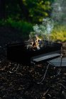 Metal griddle with burning flame of charcoal and smoke placed on ground in woods — Stock Photo