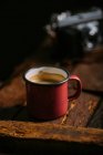 Tasse en émail de café sur une surface en bois rustique avec caméra rétro sur fond — Photo de stock