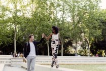Charming black woman smiling and walking on fountain border with boyfriend in park — Stock Photo
