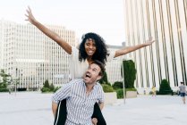Man giving piggyback ride to African-American woman while having fun on city street together — Stock Photo
