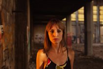 Серьезная молодая женщина, стоящая на закате в заброшенном здании — стоковое фото