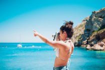 Jovem mulher tirando foto do mar na praia e apontando com a mão — Fotografia de Stock