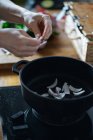 Cortar las manos femeninas cortar hojas verdes de hierbas en la tabla de cortar de madera en la mesa con estufa cerca - foto de stock