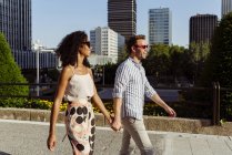 Smiling elegant multiracial couple walking holding hands in modern city — Stock Photo