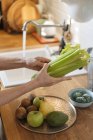 Mãos femininas lavando verduras verdes na pia abaixo do fluxo de água na cozinha — Fotografia de Stock