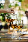 Mano umana versando vino bianco da brocca di vetro in bicchieri sul tavolo all'aperto — Foto stock