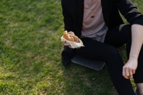 Woman sitting on grass in park and eating takeaway burger — Stock Photo