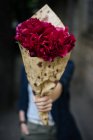 Donna in possesso di bouquet di peonie rosa in carta da regalo davanti al viso — Foto stock