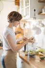 Frau steckt Zutaten in Plastikbecher mit Mixer für gesunden grünen Smoothie — Stockfoto