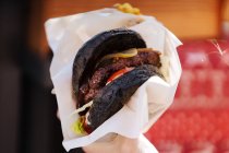 Primer plano de pan negro en hamburguesa con jugo de carne empanada y encurtidos - foto de stock