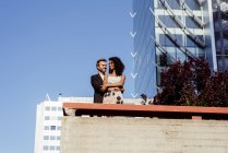 Багаторасова пара обіймається перед сучасними будівлями — стокове фото
