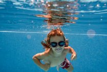 Prechooler looking in camera while swimming underwater in blue pool — стоковое фото