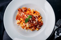 Italian pasta with meat sauce and grated cheese with potherb on white plate — Stock Photo