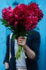 Woman holding bouquet of pink peonies in front of face on blue background — Stock Photo