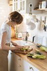 Mulher cortando maçãs e preparando prato saudável com frutas e legumes verdes no balcão de cozinha de madeira — Fotografia de Stock