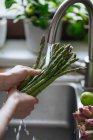 Mains féminines laver les asperges vertes fraîches dans l'évier de cuisine — Photo de stock