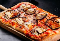 Primer plano de pizza cortada con queso, salsa y berenjenas en rodajas sobre tabla de madera sobre mesa oscura - foto de stock