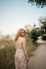 Young woman in dress looking over shoulder on countryside road — Stock Photo
