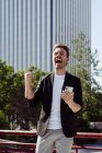 Homme excité tenant smartphone et se réjouissant de la victoire tout en se tenant sur la rue de la ville moderne — Photo de stock