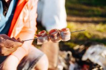 Main humaine tenant bandelettes de bacon pliées sur brochette métallique pour repas barbecue — Photo de stock