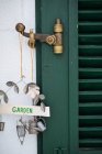 Close-up view of old rustic green wooden door with worn bronze latch and beautiful metal garden sign with watering can and bucket figurines hanging from it at white plastered wall — Stock Photo