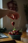 Human hand elegantly taking stem of ripe juicy strawberry from bowl of berries on wooden table — Stock Photo