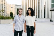 Portrait of cheerful couple holding hands in front of modern buildings — Stock Photo