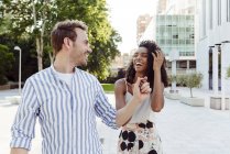Couple riant tenant la main tout en marchant dans le parc de la ville — Photo de stock