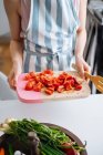 Gros plan des mains féminines tenant la planche à découper avec des tranches de poivrons rouges et de tomates dans la cuisine — Photo de stock