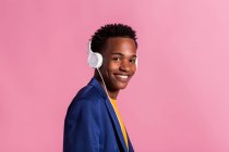 Portrait of young black man in jacket and headphones smiling at camera on pink background — Stock Photo