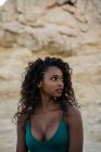 Portrait of beautiful woman with curls standing against rocks — Stock Photo