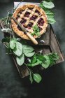Flat lay of baked cherry pie with lattice crust served on wooden box among green leaves — Stock Photo
