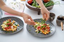 Menschenhände bestreuen Zwiebelomelette mit Gemüse auf Teller — Stockfoto
