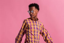 Elegante hipster en gafas de sol y camisa a cuadros sobre fondo rosa - foto de stock