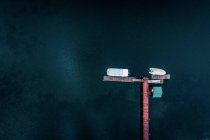 Вид с воздуха на небольшие лодки, пристыкованные к деревянной посадочной платформе в окружении красивой глубокой темной поверхности океана — стоковое фото