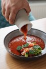 Close-up of human hand pouring traditional Nordic red soup garnished with herbs in bowl — Stock Photo