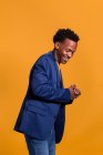 Dandy black man in jacket and jeans laughing on orange background — Stock Photo