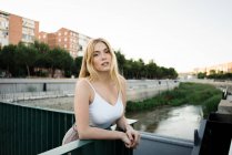Portrait of young woman leaning on bridge railing in city — Stock Photo
