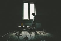 Silhouette of man in hat standing near windows in dirty room with rubbish. — Stock Photo