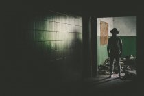 Figura maschile scura in cappello in piedi in un vecchio edificio abbandonato . — Foto stock