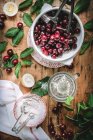 Flat lay of cherries and cherry pitter composed with green leaves, flour and lemon on rustic table — Stock Photo