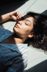 Young pensive brunette woman with long hair lying on floor in shadow and sunlight — Stock Photo