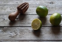 Limas frescas enteras y cortadas a la mitad con exprimidor de madera sobre madera gris - foto de stock